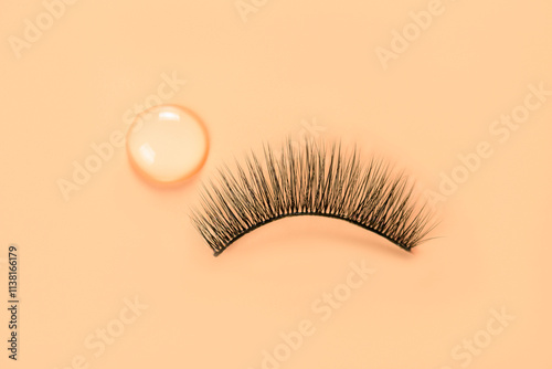 False eyelash and drop of glue on orange background. Women beauty and eyelash extensions.