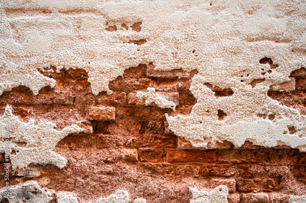 Brick wall with pieces of plaster. Wall of an old building in need of renovation. Aged wall texture of brick building close up. Grunge background with red and white blocks and layers of cement stucco