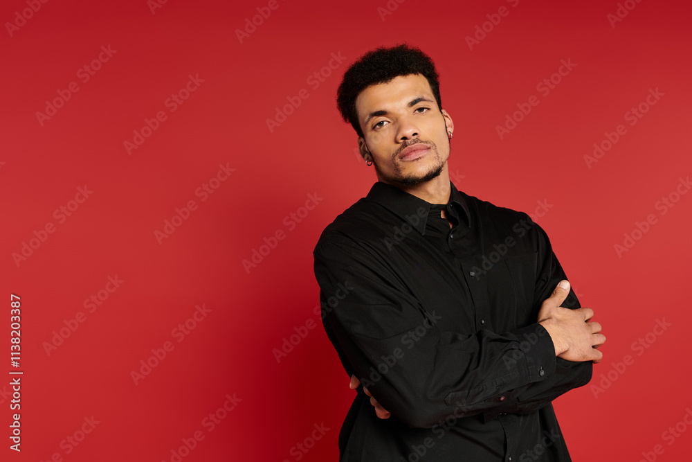 Young man in a black outfit stands confidently with arms crossed against a red background. Young man in a black outfit stands confidently with arms crossed against a red background.