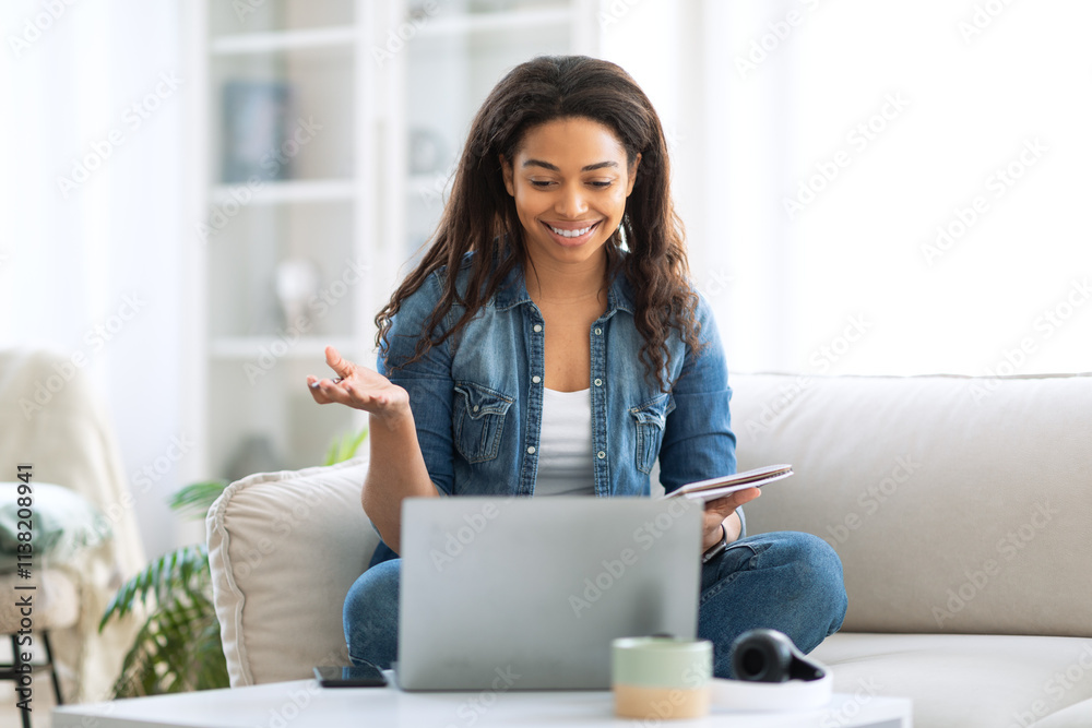 A woman sits comfortably on a sofa, interacting with her laptop while smiling. She is actively participating in a virtual meeting with her tablet close by, showcasing a cozy home environment. A woman sits comfortably on a sofa, interacting with her laptop while smiling. She is actively participating in a virtual meeting with her tablet close by, showcasing a cozy home environment.