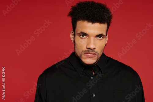 A young handsome man dressed in black stands confidently in front of a vibrant red background. photo