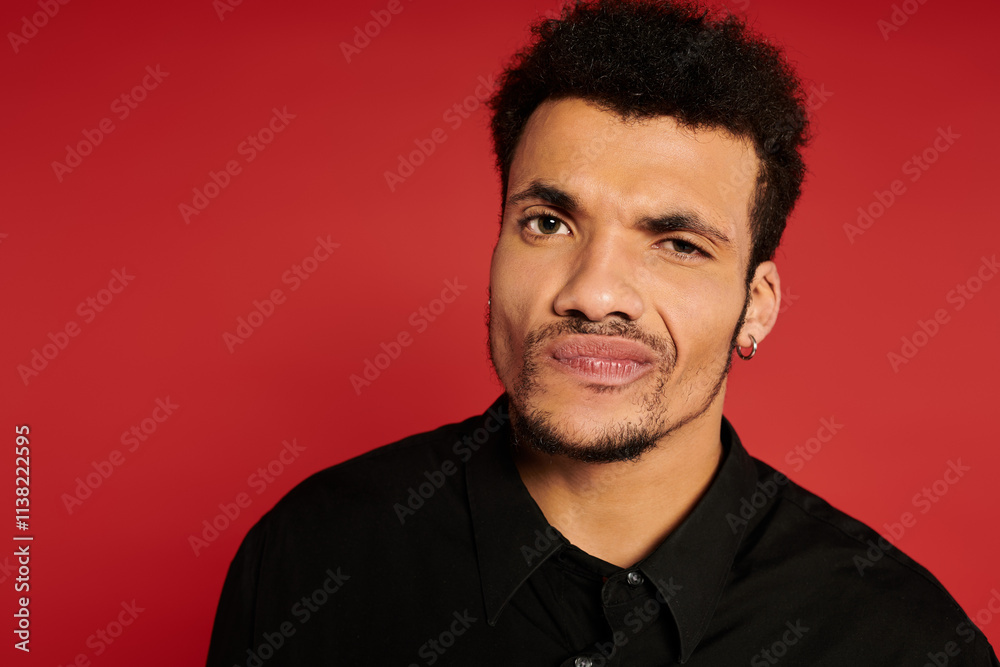 A young handsome man displays a playful expression against a vibrant red backdrop. A young handsome man displays a playful expression against a vibrant red backdrop.