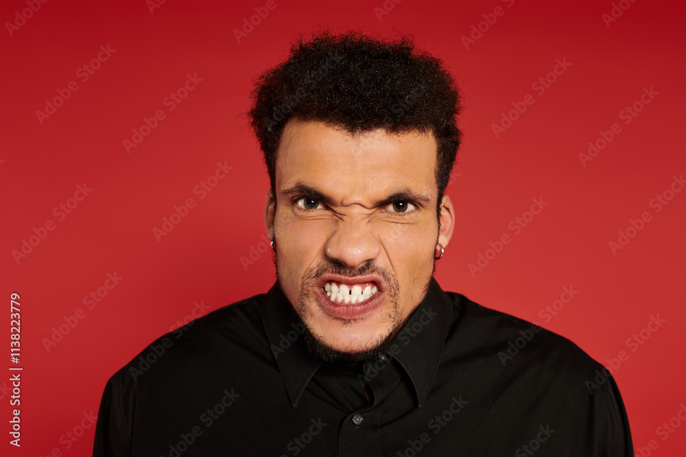 A young handsome man with curly hair displays a fierce expression against a red backdrop. A young handsome man with curly hair displays a fierce expression against a red backdrop.