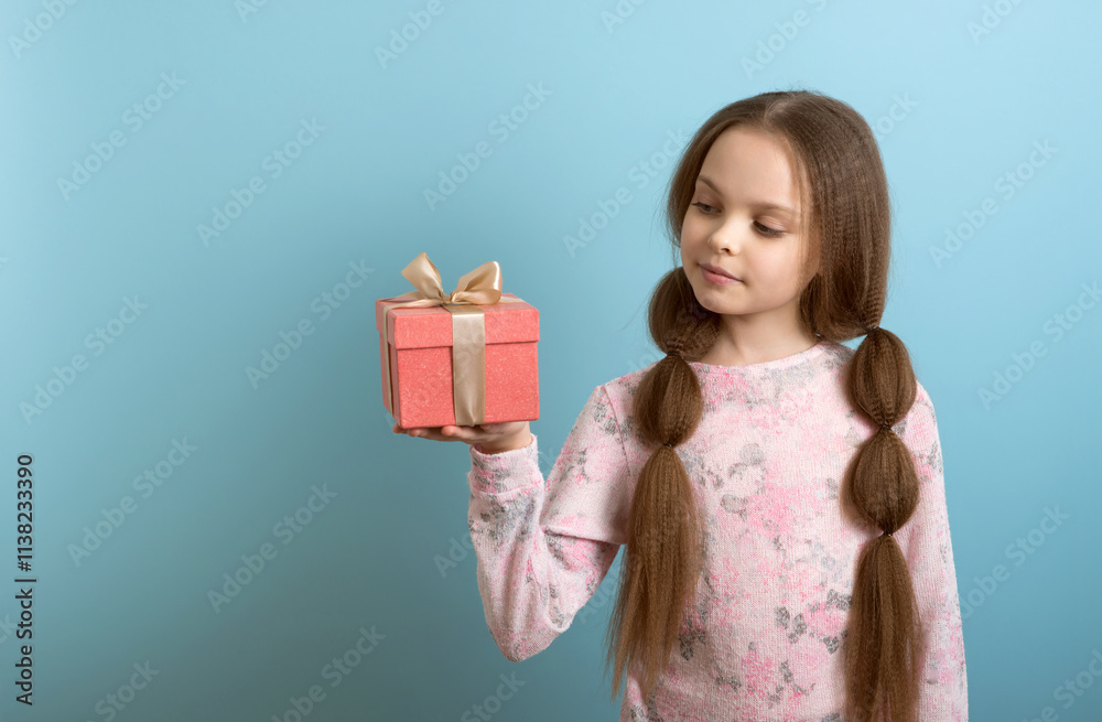 Cute little girl in winter clothes posing on light background with gift box in hand. Christmas and New year waiting and celebration concept. Cute little girl in winter clothes posing on light background with gift box in hand. Christmas and New year waiting and celebration concept.