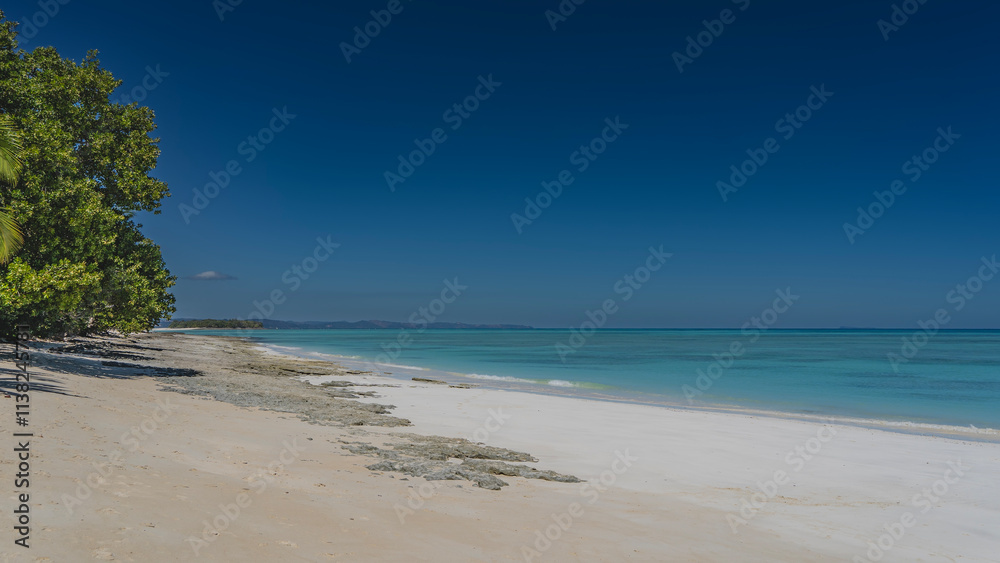 A beautiful tropical beach, without people. A calm turquoise ocean. The blue sky. The tropical trees bent down. Shadows on the white sand. Copy space. Madagascar. Nosy Iranja A beautiful tropical beach, without people. A calm turquoise ocean. The blue sky. The tropical trees bent down. Shadows on the white sand. Copy space. Madagascar. Nosy Iranja