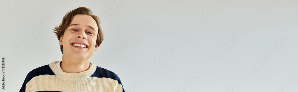 A cheerful young student wears a striped sweater while enjoying his college experience in a studio, banner
