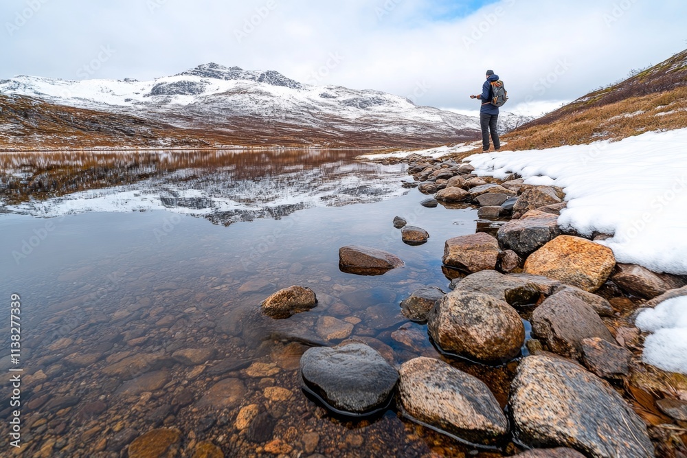 Fototapeta premium A person standing by the edge of a fjord, skipping stones across the smooth, reflective water