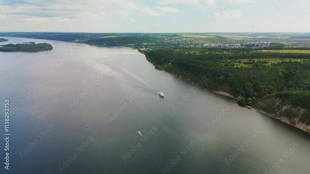the ship is moving along the river, forming waves behind it. Top view of the wide river, forest and fields the ship is moving along the river, forming waves behind it. Top view of the wide river, forest and fields