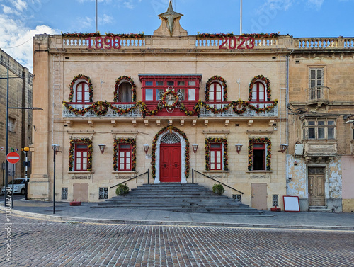 Historic Maltese building adorned with Christmas garlands and wreaths, featuring striking red accents and heritage architecture photo