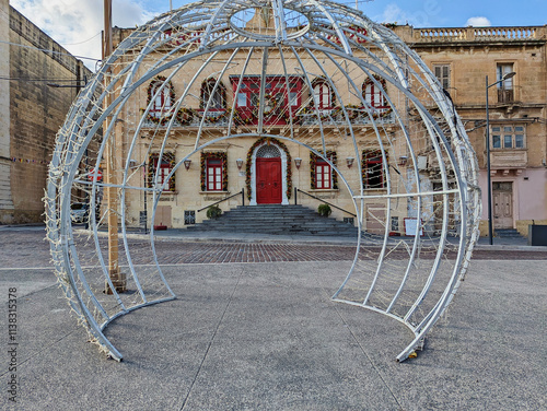 Christmas light installation opposite historic Maltese building adorned with festive wreaths and red accents, creating holiday scene photo