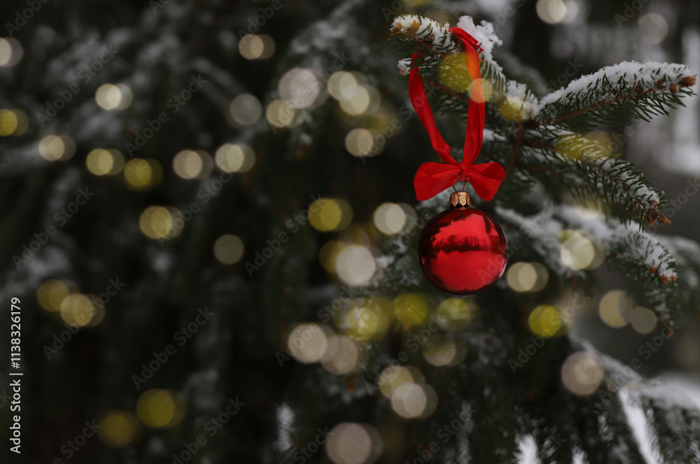 Obraz premium red New Year's ball with a red bow on a snow-covered Christmas tree
