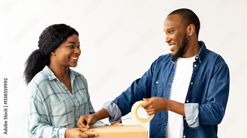 Joyful Black Spouses Moving To New Home, Packing Belongings In Cardboard Boxes, Happy Young African American Couple Using Scotch Tape To Close Package And Smiling To Each Other, Closeup Shot Joyful Black Spouses Moving To New Home, Packing Belongings In Cardboard Boxes, Happy Young African American Couple Using Scotch Tape To Close Package And Smiling To Each Other, Closeup Shot
