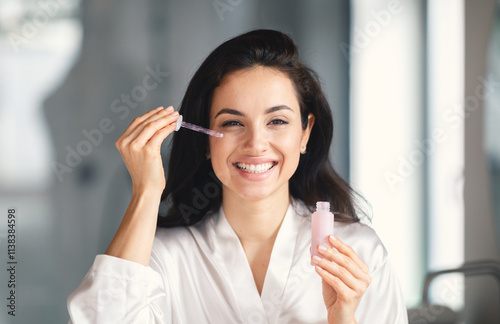 A young Caucasian woman is smiling while applying a serum in her home bathroom. She enjoys her skincare routine  radiating beauty and confidence.