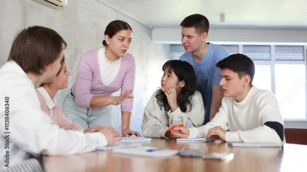 Smiling motivated young female team leader holding meeting with group of fellow students, explaining details of new study project Smiling motivated young female team leader holding meeting with group of fellow students, explaining details of new study project