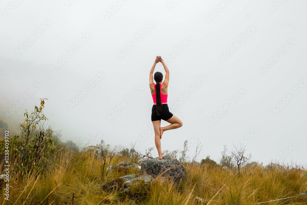 Joven atractiva practicando yoga al aire libre rodeada de naturaleza y nubes, simbolizando un estilo de vida saludable y equilibrio interior Joven atractiva practicando yoga al aire libre rodeada de naturaleza y nubes, simbolizando un estilo de vida saludable y equilibrio interior