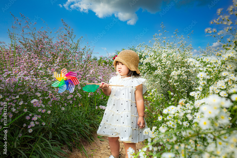 Happy girl standing in a flower garden with a toy windmill,Asian little girl holding a windmill running in a flower field Happy girl standing in a flower garden with a toy windmill,Asian little girl holding a windmill running in a flower field