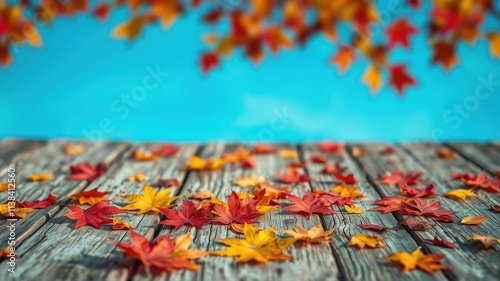 Autumn leaves scattered on a wooden surface with a blurred background of a blue sky and more leaves