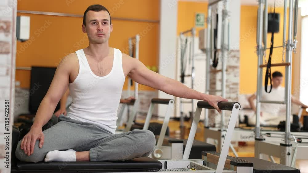 Man in gym with help of rope reformer performs exercises to strengthen muscles of her arms. Pilates sports club, classes and simulators, body shape Man in gym with help of rope reformer performs exercises to strengthen muscles of her arms. Pilates sports club, classes and simulators, body shape
