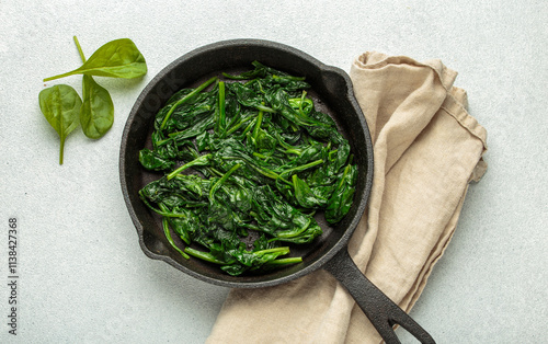 Freshly steamed spinach leaves are served in a cast iron pan, resting on a beige napkin, healthy eating and vibrant green vegetables