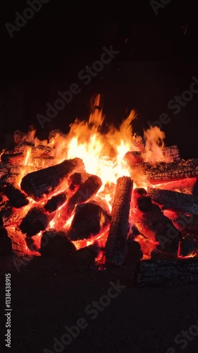 Bonfire made of logs burning with hot flames, with sparks flying. Bonfire isolated in the darkness. Vertical video.