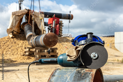 Ein Schleifgerät liegt auf einem Rohr auf einer Baustelle. Im Hintergrund wird ein Rohr mit einem Kran in Position gebracht