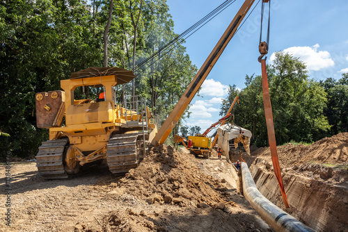 Auf der Baustelle werden Rohre mit Hilfe eines Krans verlegt. Bauarbeiter beaufsichtigen die Montage und Positionierung der großen Rohre in einem tiefen Graben