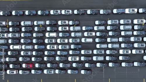 Aerial view of new electric cars on a huge dealership parking lot. New unsold cars in storage at the automotive plant. Motion over rows of finished cars at huge open warehouse ground of giant plant