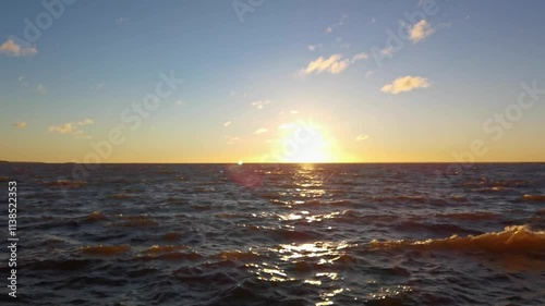 Golden sunset over expansive ocean waves with clouds in a tranquil evening sky.