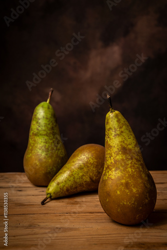 View of three pears on a wooden table, brown background, vertical with copy space