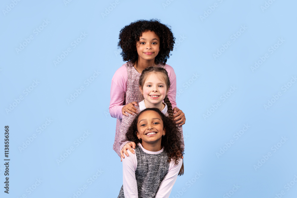 Three happy preteen girls stand against a blue background, smiling and showcasing their friendship. Their diverse backgrounds highlight the joy of childhood and togetherness. Three happy preteen girls stand against a blue background, smiling and showcasing their friendship. Their diverse backgrounds highlight the joy of childhood and togetherness.