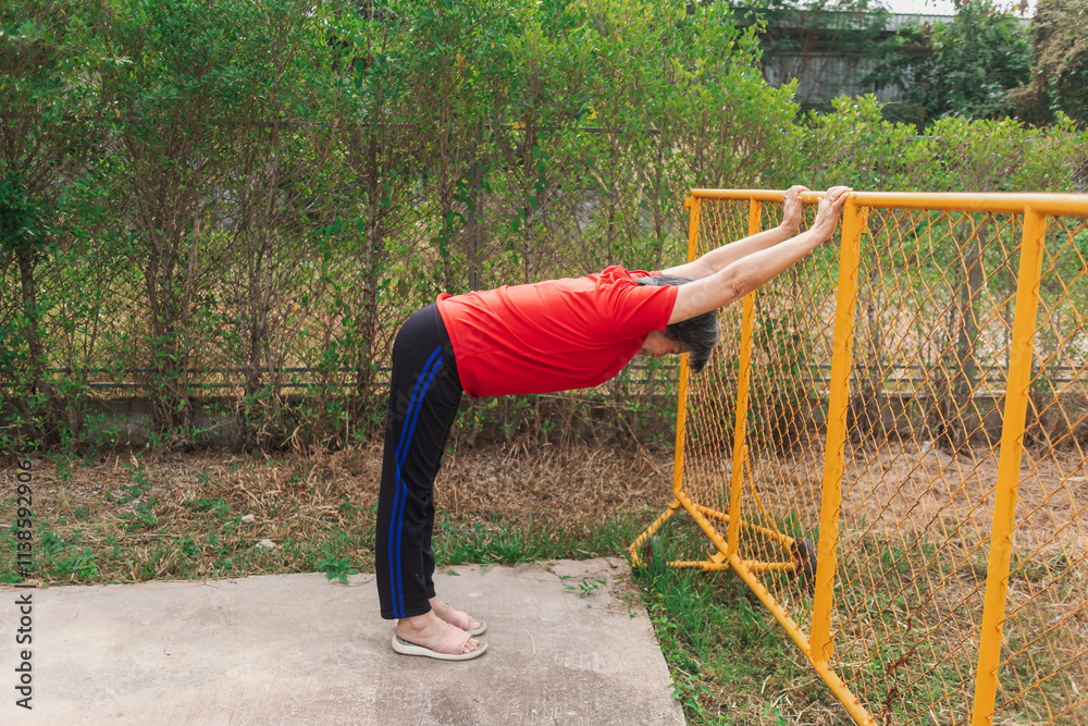Fototapeta premium Happy asian old woman stretching arms and body at park in morning after exercise, wear red t-shirt, healthy routine.