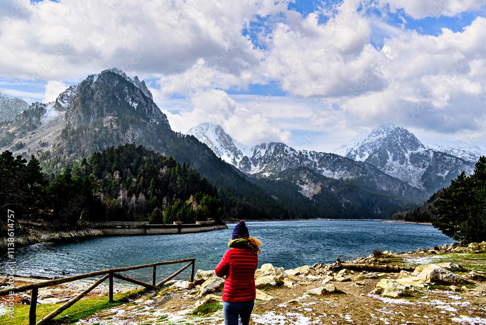 Woman in red coat at Sant Maurici Lake with snowy mountains, in Aigües Tortes National Park, in the Pyrenees of Lleida, Catalonia, Spain Woman in red coat at Sant Maurici Lake with snowy mountains, in Aigües Tortes National Park, in the Pyrenees of Lleida, Catalonia, Spain