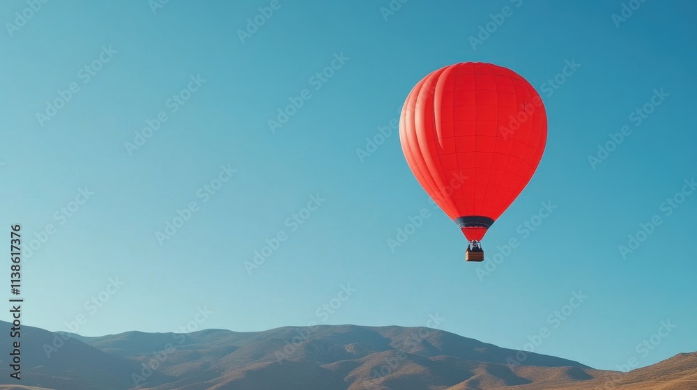 Bright Red Hot Air Balloon Floating in Clear Blue Sky Over Mountain Landscape Bright Red Hot Air Balloon Floating in Clear Blue Sky Over Mountain Landscape