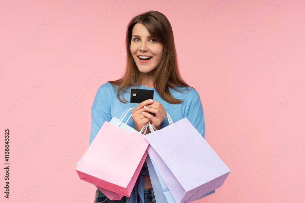 Studio shot of excited attractive young woman posing with shopping bags and credit card in hands, isolated over pastel pink background Studio shot of excited attractive young woman posing with shopping bags and credit card in hands, isolated over pastel pink background