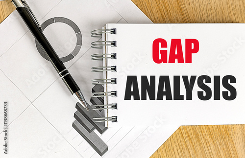 Notebook with the words gap analysis on a desk with charts, a black pen, and wooden background