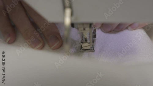 This video shows a close up view of stitcher's hands passing white fabric through a sewing machine.