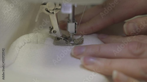 This close up, side view video shows skilled stitcher hands sewing a seam of white upholstery fabric on a sewing machine. 