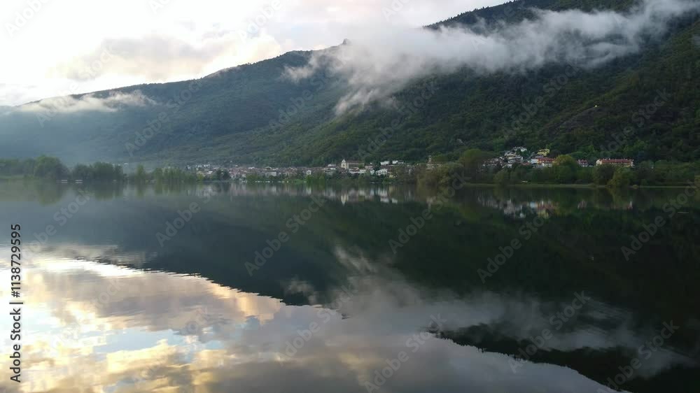 Drone view of Revine Lake with tranquil water reflecting the sky, mountain and a peaceful town Drone view of Revine Lake with tranquil water reflecting the sky, mountain and a peaceful town