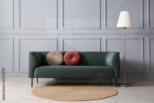 Comfortable sofa and lamp near grey wall in room