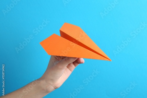 Woman with handmade paper plane on light blue background, closeup