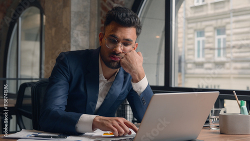 Tired stressed sad male guy Arabian man office employee tap keyboard on laptop boring online work in office alone Indian businessman exhausted lazy burnout overwork headache stress business problem photo