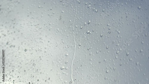 Experience the beauty of rainy weather as raindrops cascade down a window in stunning close-up. Perfect for conveying emotions of calmness, nostalgia, and the soothing sound of rain