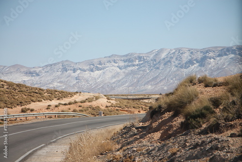 A road meandering through the mountains through a snowy landscape with blue sky and sun