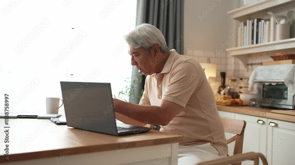 Senior business man working on laptop while checking at document at home. Middle aged manager writing report and looking at financial chart by using computer while sitting at living room. Myrmidon. Senior business man working on laptop while checking at document at home. Middle aged manager writing report and looking at financial chart by using computer while sitting at living room. Myrmidon.