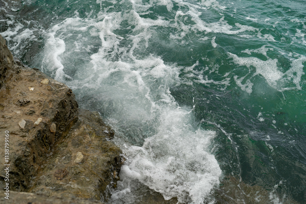 Fototapeta premium Surfing waves hit the rugged coastline, creating foam and splashes in a tropical paradise.