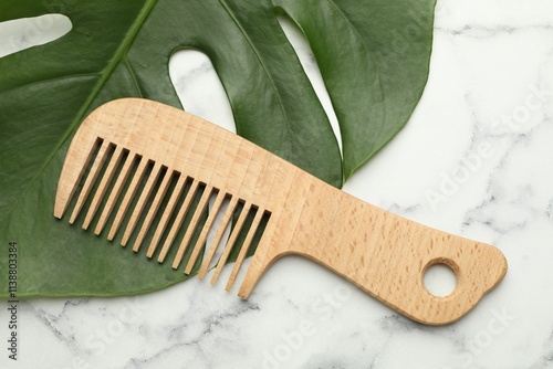 Wooden comb and monstera leaf on white marble table, flat lay