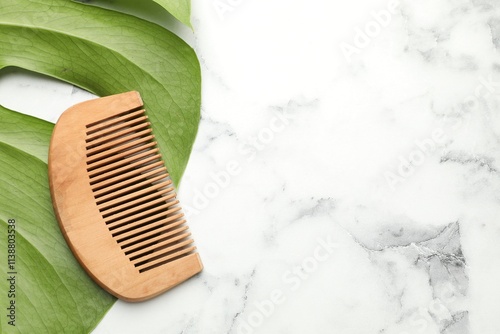 Bild auf Leinwand Wooden comb and monstera leaf on white marble table, top view