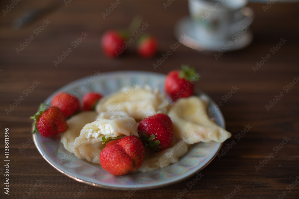A plate of dumplings with strawberries served on a wooden table, dusted with powdered sugar. A cup of tea in a vintage porcelain cup adds a touch of elegance to this homemade meal.
A plate of dumplings with strawberries served on a wooden table, dusted with powdered sugar. A cup of tea in a vintage porcelain cup adds a touch of elegance to this homemade meal.