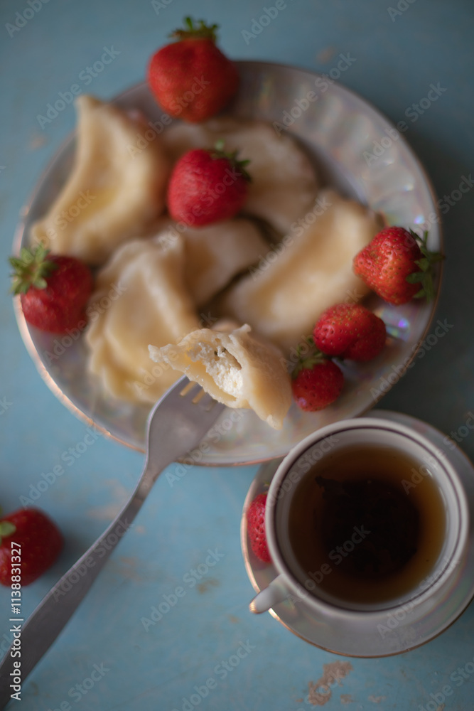 A plate of sweet dumplings with strawberries on a light blue table, with a bite taken out to reveal the creamy filling. A cup of tea sits nearby, completing the relaxing scene.
A plate of sweet dumplings with strawberries on a light blue table, with a bite taken out to reveal the creamy filling. A cup of tea sits nearby, completing the relaxing scene.