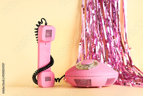 Pink retro telephone with tinsel on beige background